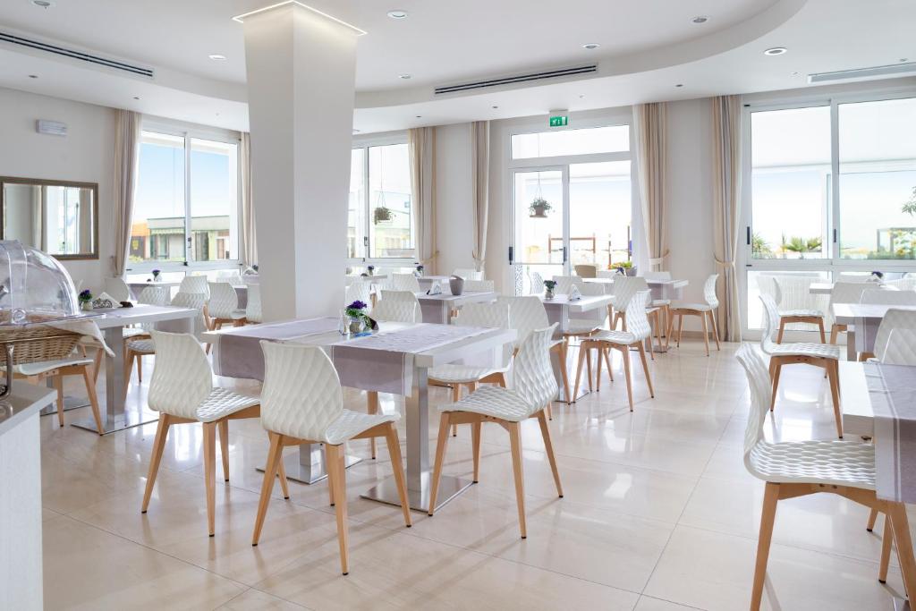 un restaurant avec des tables et des chaises blanches et des fenêtres dans l'établissement Hotel Riviera, à Bellaria-Igea Marina