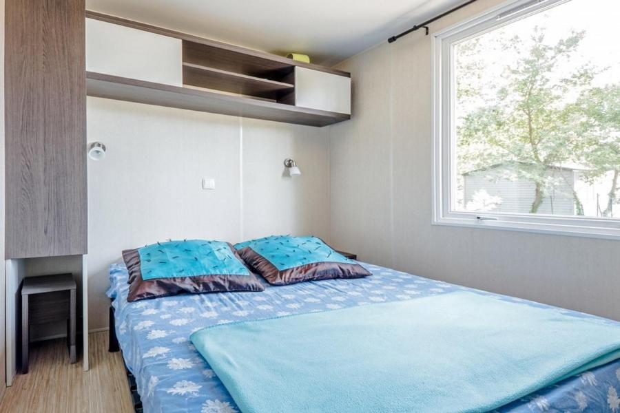 une chambre avec un lit avec des draps bleus et une fenêtre dans l'établissement Camping Taxo Les Pins - Maeva, à Argelès-sur-Mer 31 autres photos