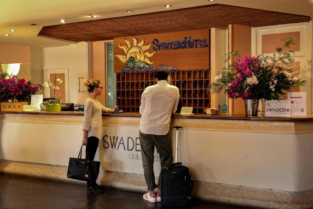 un homme et une femme debout à un comptoir dans l'établissement Swadeshi Sporting Hotel Tanca Manna, à Cannigione