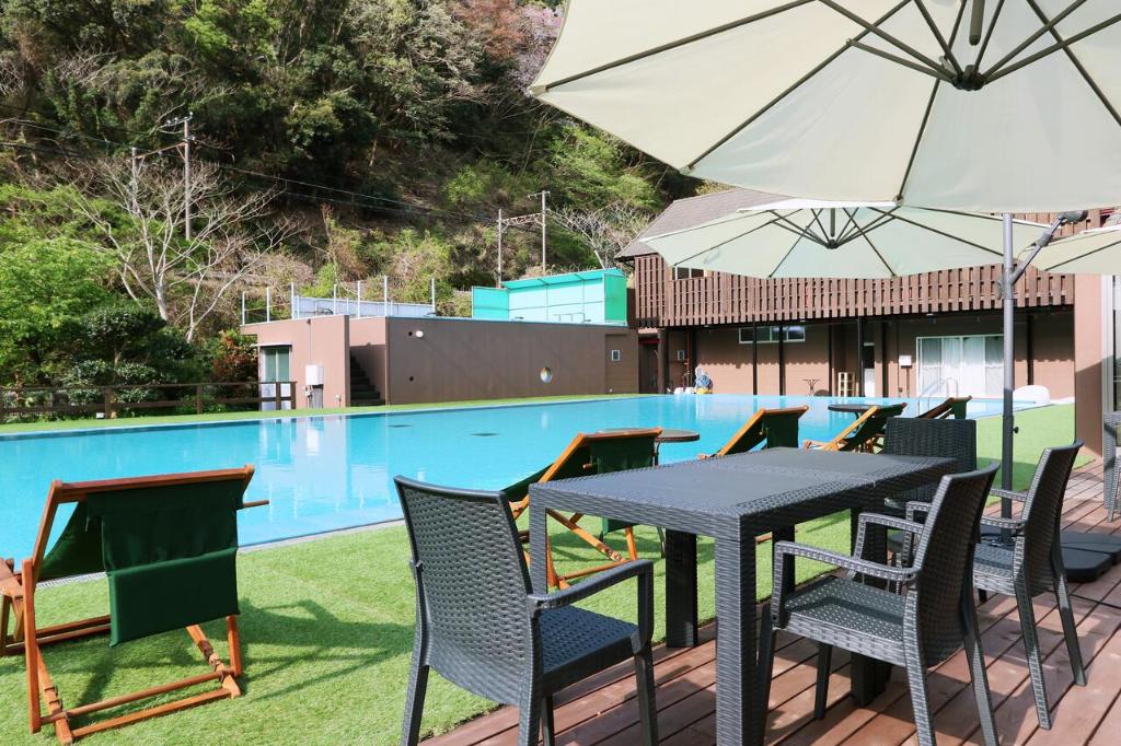 - une table et des chaises avec un parasol à côté de la piscine dans l'établissement Amis Droles アミドローラ LIBERTY RESORT, à Kawazu
