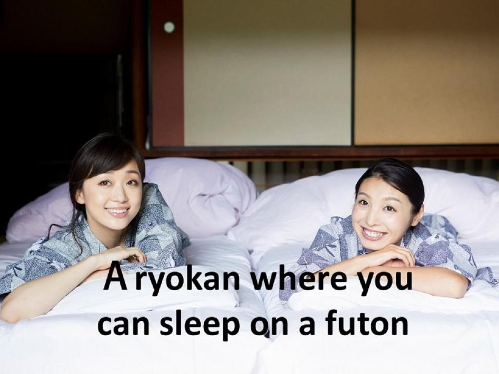 Deux filles qui se couchent sur le lit avec les mots un kyrkan où vous pouvez dormir dans l'établissement Ryokan with natural hot springs and okonomiyaki Miyajima-an Hiroshima, à Miyajima