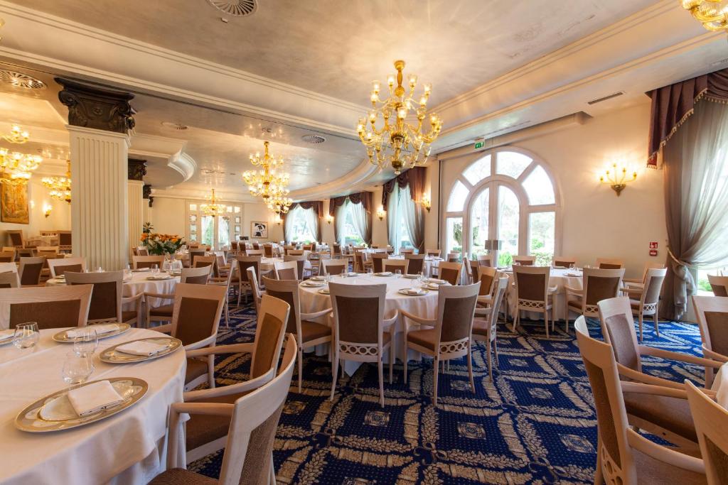 un restaurant avec des tables et des chaises blanches et un lustre dans l'établissement Palace Hotel, à Milano Marittima