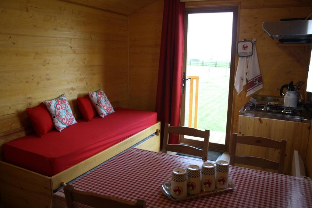 Cette petite chambre comprend un lit rouge avec une table et une fenêtre. dans l'établissement Roulotte Poulette, à Mortagne-au-Perche