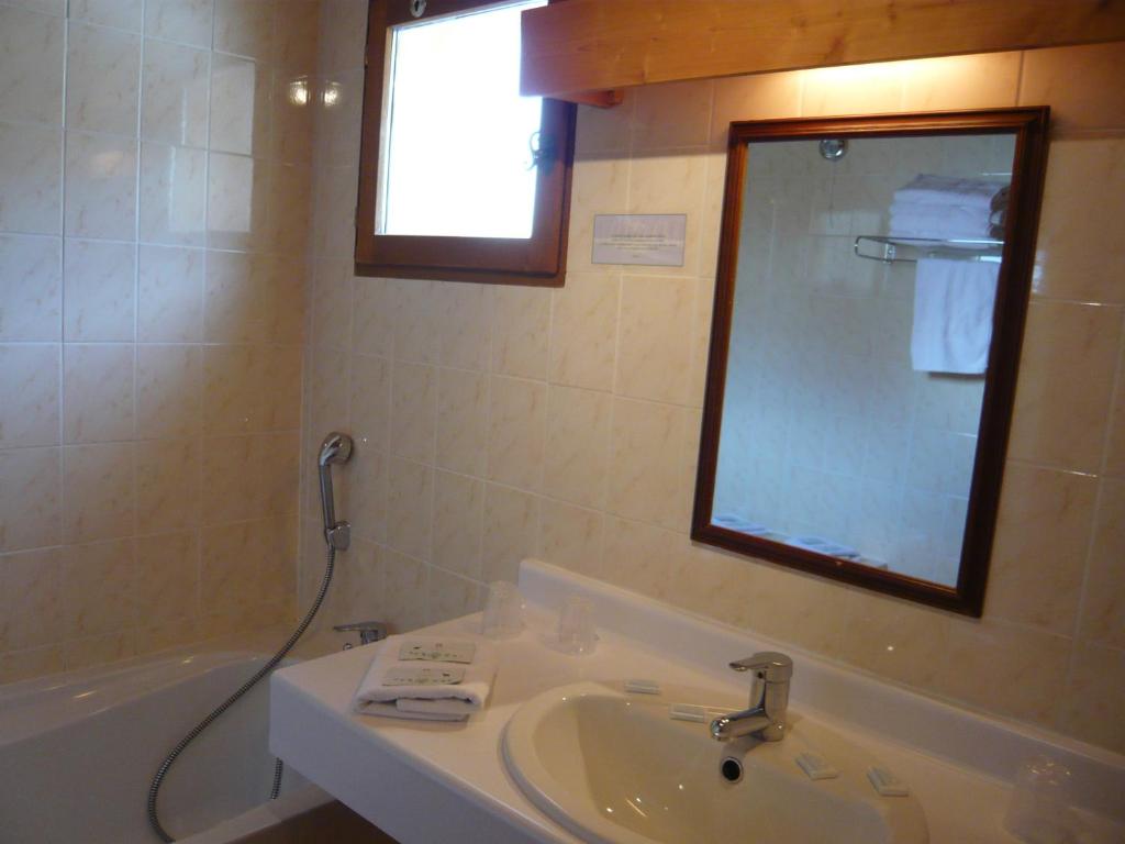 une salle de bain avec un lavabo, une baignoire et un miroir dans l'établissement Hotel Le Tetras, à Notre-Dame-de-Bellecombe