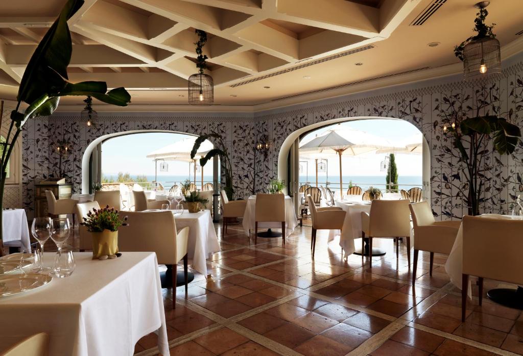 un restaurant avec des tables et des chaises blanches et des fenêtres dans l'établissement Il Pellicano, à Porto Ercole
