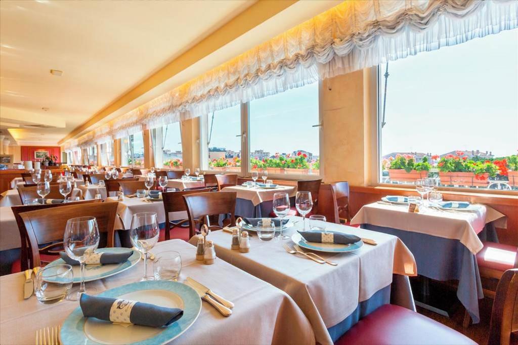un restaurant avec des tables et des chaises blanches et des fenêtres dans l'établissement Hotel Principe Palace, à Lido di Jesolo