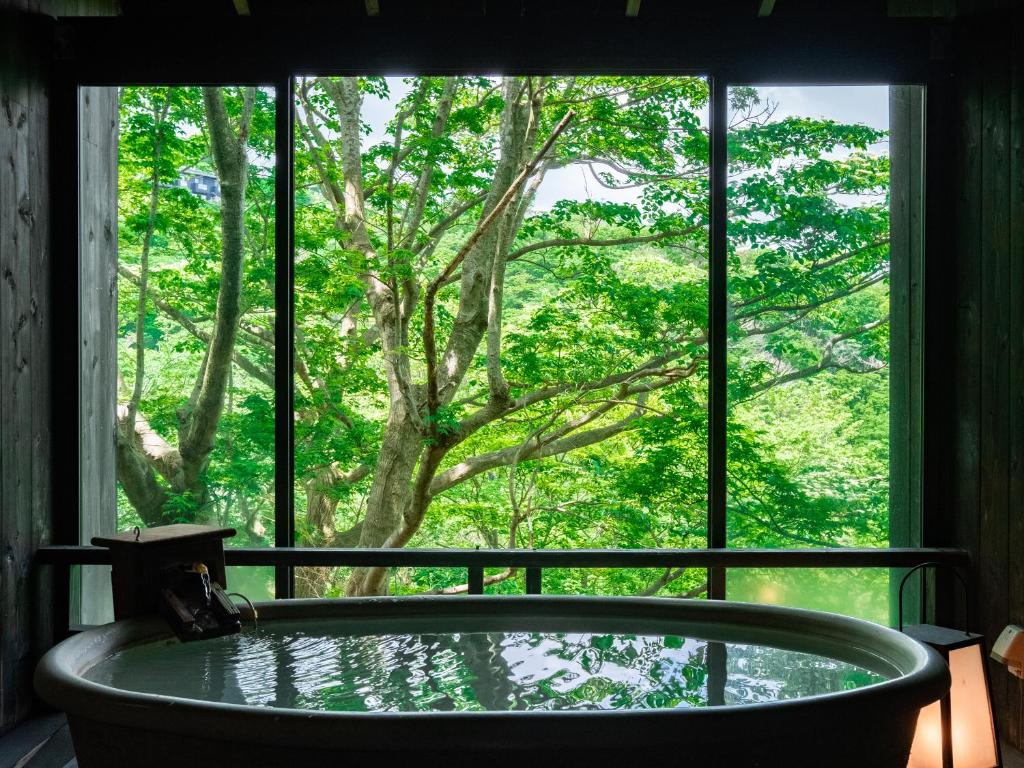 une baignoire en face d'une fenêtre avec un arbre dans l'établissement Nagominoyado Hanagokoro - Reopening in Mar 2024, à Hakone