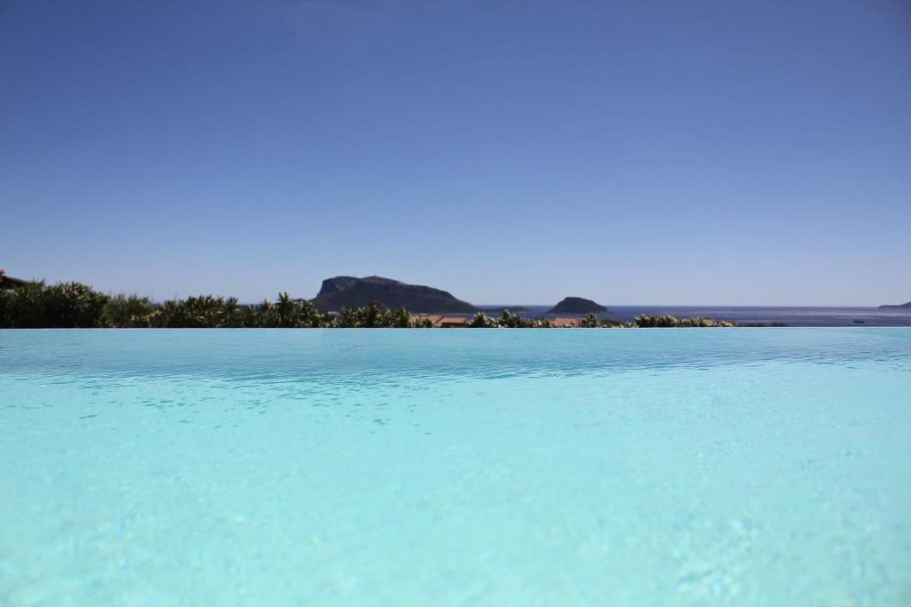 une grande piscine d'eau bleue avec des montagnes en arrière-plan dans l'établissement VILLA ALBA NUOVA with infinity pool & amazing sea view, à Golfo Aranci 32 autres photos