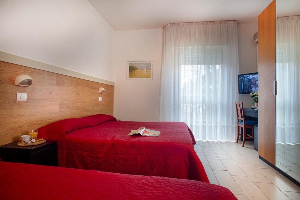 une chambre d'hôtel avec deux lits rouges et une table dans l'établissement Club Hotel Angelini, à Bellaria-Igea Marina