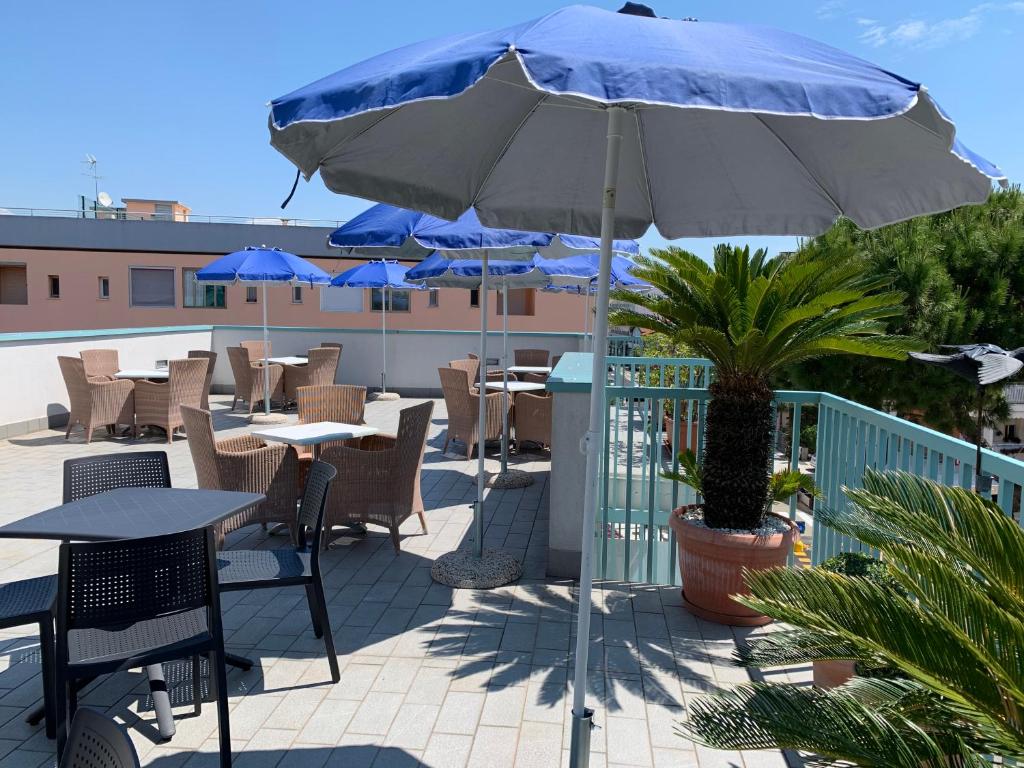 un patio avec tables, chaises et un parasol dans l'établissement Hotel Raffaello, à Caorle
