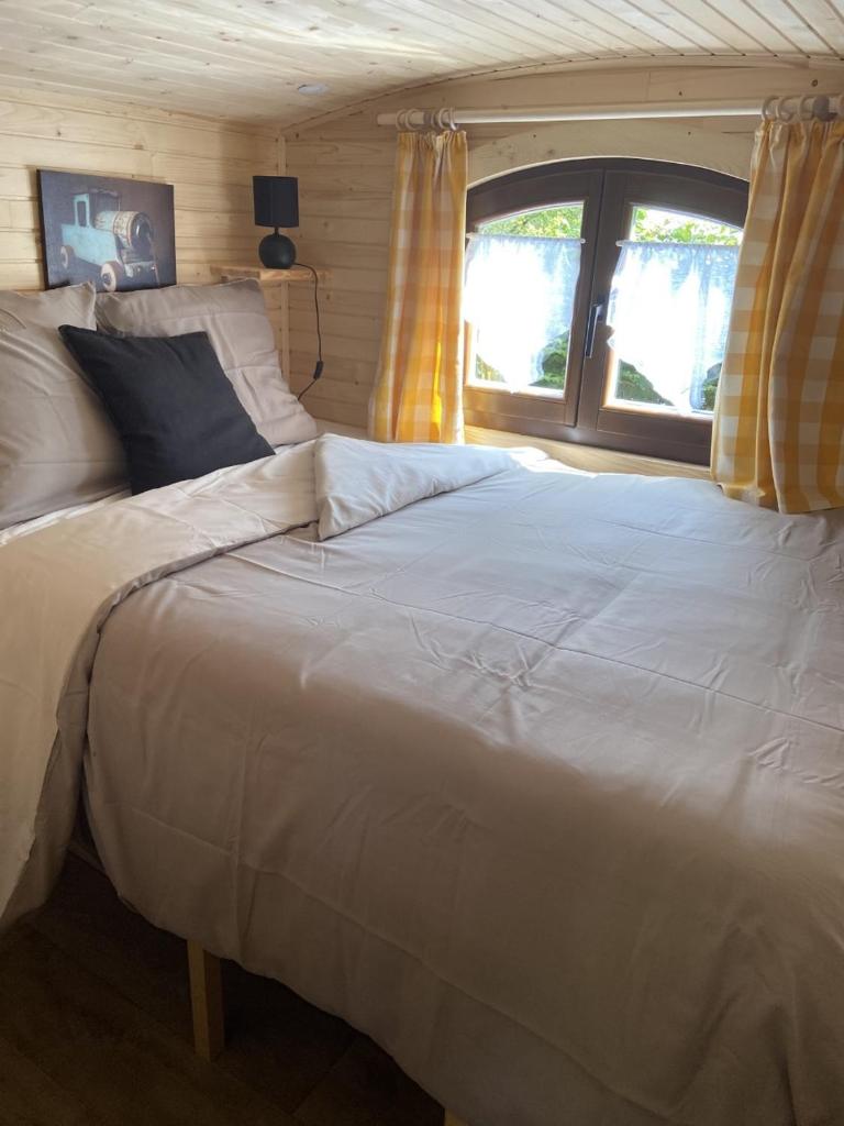 un grand lit blanc dans une chambre avec une fenêtre dans l'établissement La Roulotte d'Emilie et son jacuzzi privé, à Beurlay