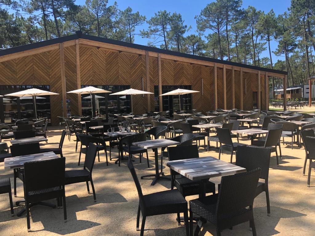 un restaurant vide avec des tables, des chaises et des parasols dans l'établissement Mobile Home - Les Dunes de Contis, à Saint-Julien-en-Born