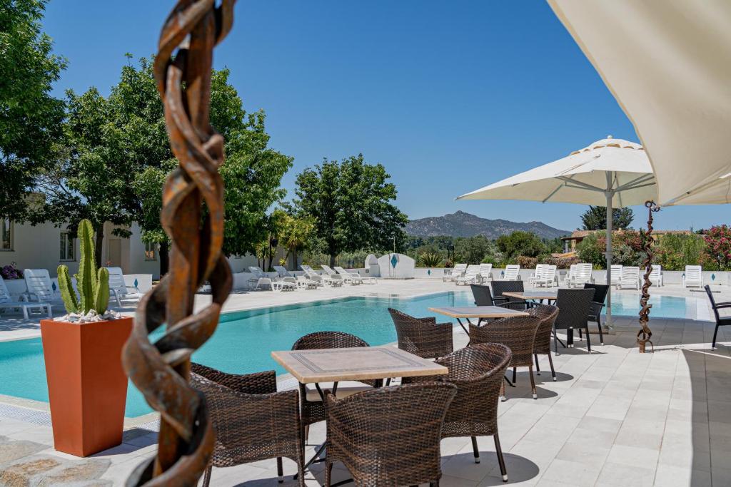 un patio avec tables et chaises à côté d'une piscine dans l'établissement Hotel Le Mimose, à San Teodoro