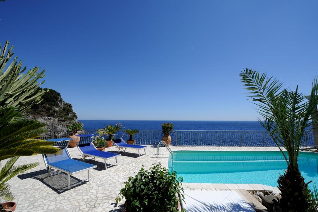 une piscine avec des chaises et l'océan en arrière-plan dans l'établissement Villa Azzurra, à Conca dei Marini