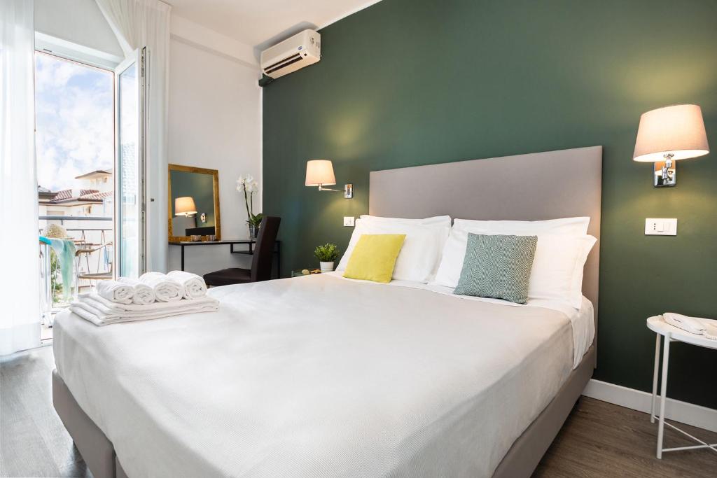 Cette chambre comprend un grand lit blanc et un mur vert. dans l'établissement Hotel Aurora, à Lignano Sabbiadoro
