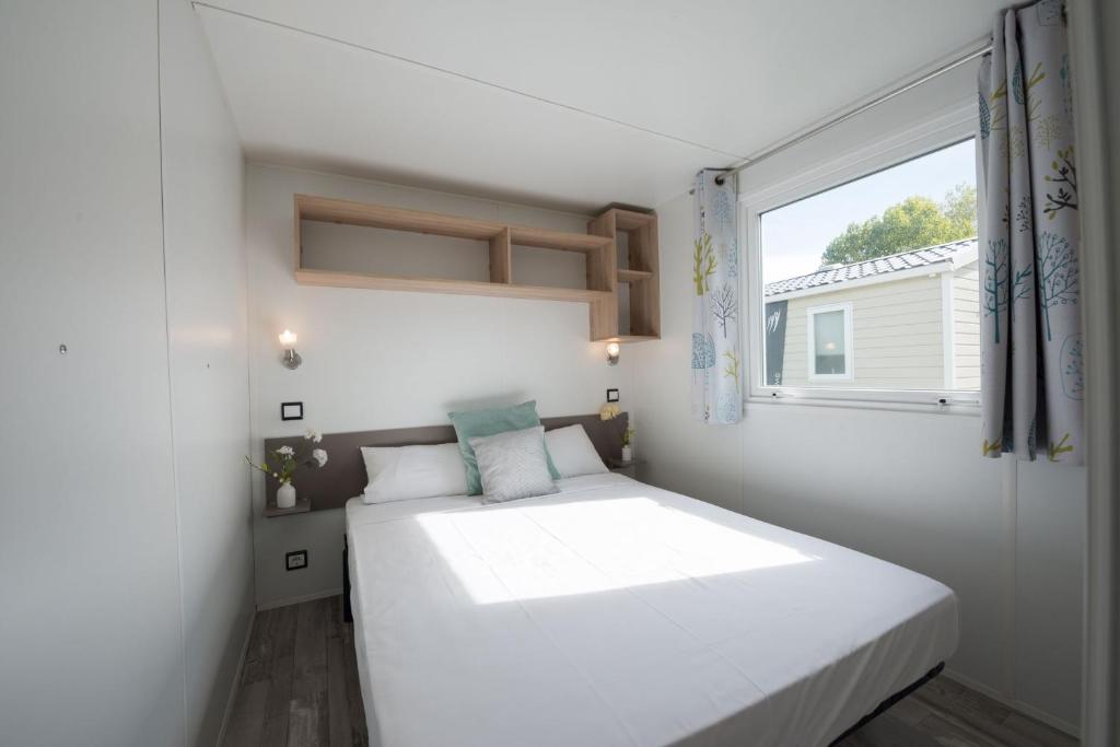 une petite chambre avec un lit blanc et une fenêtre dans l'établissement Camping Aux Rives du Soleil, à Pont-de-Vaux