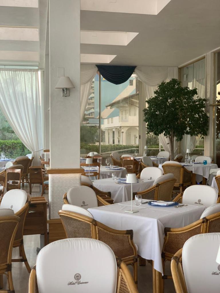 un restaurant avec des tables et des chaises blanches et des fenêtres dans l'établissement Hotel Universo, à Lido di Jesolo
