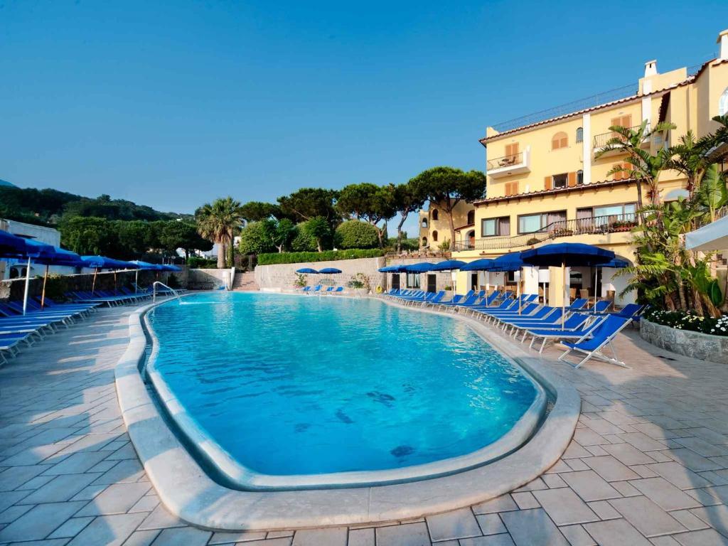 une grande piscine avec des chaises et des parasols bleus dans l'établissement Hotel San Lorenzo Thermal Spa, à Ischia