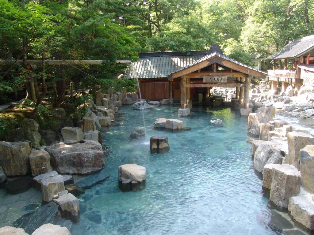 une piscine d'eau bleue avec des rochers et un bâtiment dans l'établissement Takaragawa Onsen Ousenkaku, à Minakami