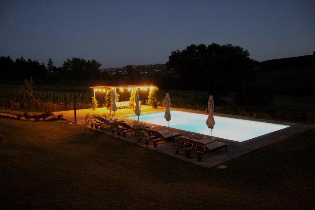 - une piscine avec des tables et des parasols la nuit dans l'établissement Villa La Mura - Luxury Pool by the Vineyard, à Costigliole dʼAsti