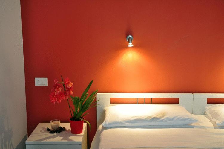 - une chambre avec un mur orange, un lit et un vase de fleurs dans l'établissement Hotel La Punta, à Otrante