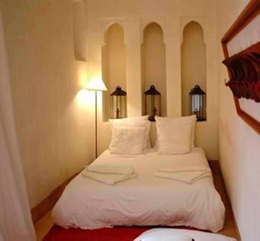 une chambre avec un lit avec des draps blancs et des oreillers dans l'établissement Riad La Perle de Marrakech, à Marrakech