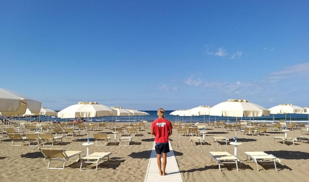 un homme debout sur une plage avec des chaises et des parasols dans l'établissement Hotel Miramare, à Castiglione della Pescaia 184 autres photos