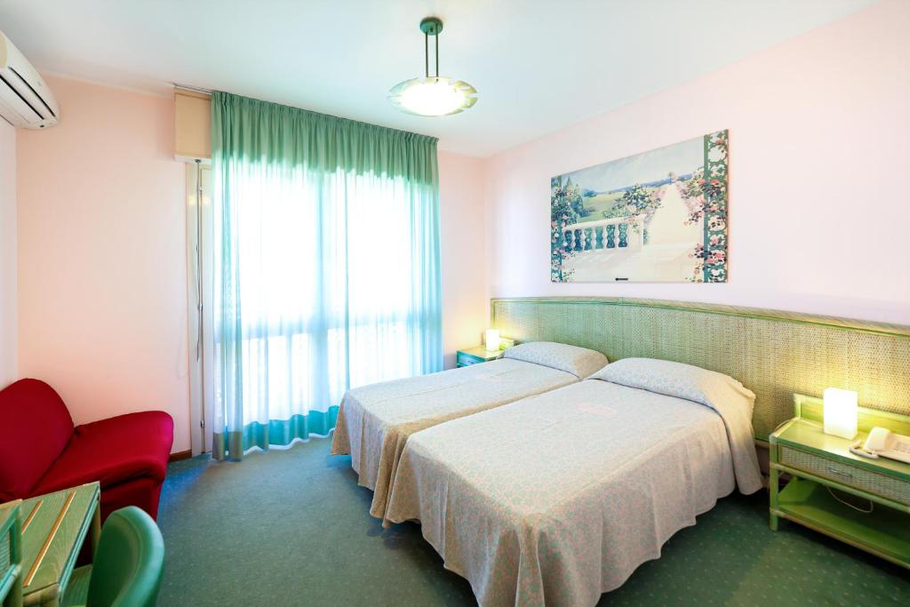 une chambre d'hôtel avec deux lits et une chaise rouge dans l'établissement Hotel American, à Lignano Sabbiadoro 45 autres photos
