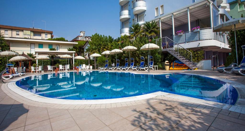une piscine avec chaises et parasols à côté d'un bâtiment dans l'établissement Hotel Helios, à Lido di Jesolo