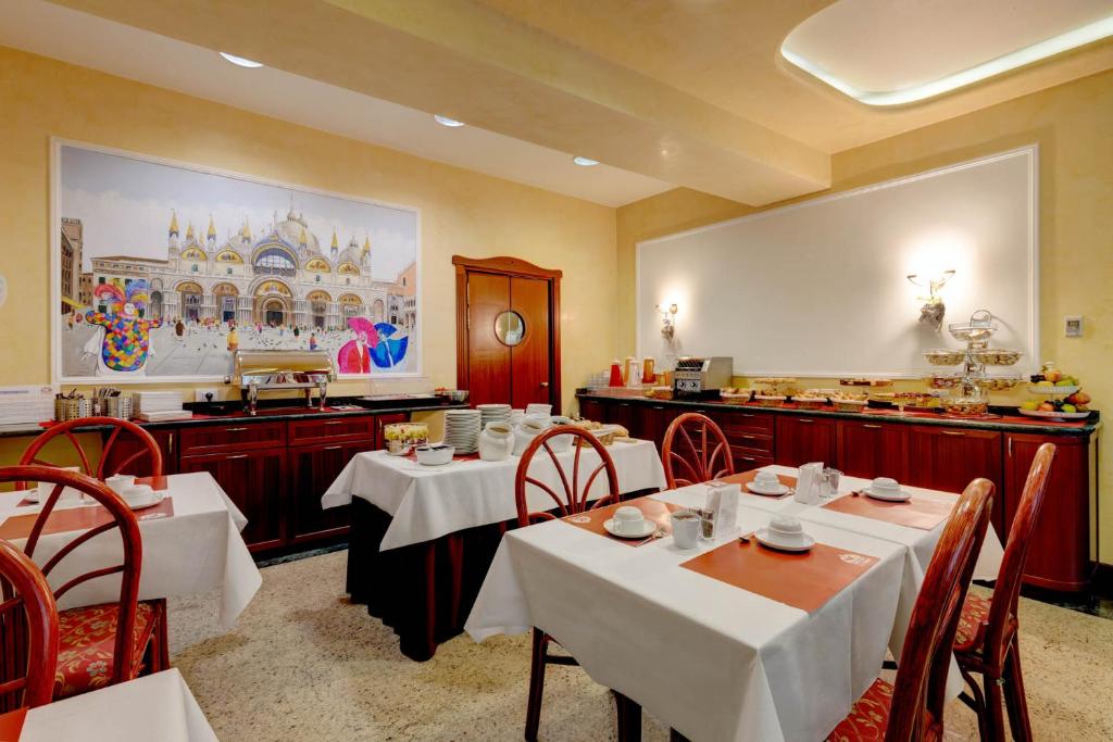 un restaurant avec des tables et des chaises blanches dans une salle dans l'établissement Hotel Garni San Carlo, à Lido di Jesolo