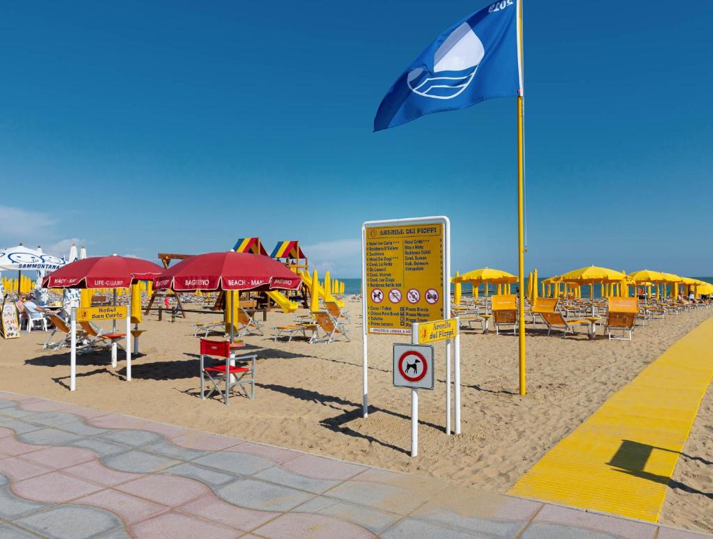 une plage de sable avec des parasols, des chaises et un drapeau dans l'établissement Hotel Garni San Carlo, à Lido di Jesolo