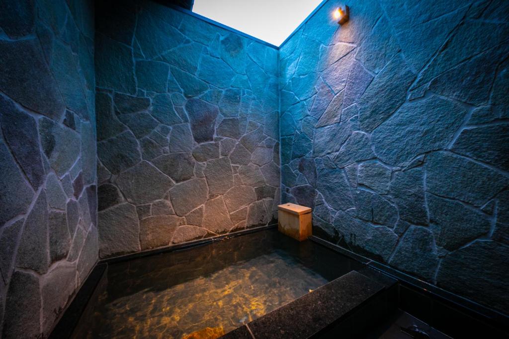 La salle de bains est pourvue d'une baignoire et d'un mur en pierre bleue. dans l'établissement Yufuin Kaze no Mori, à Yufu