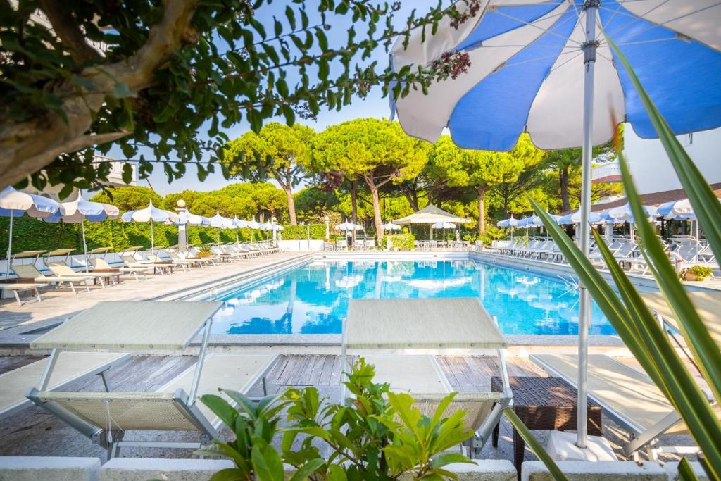 une piscine avec des chaises et un parasol dans l'établissement Hotel Al Cigno, à Lignano Sabbiadoro