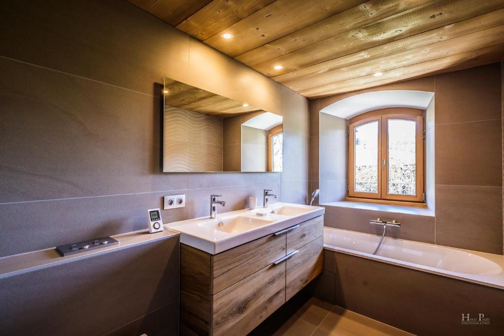 une salle de bain avec un lavabo, une baignoire et un miroir dans l'établissement Ski in ski out Le Moulin charming duplex just 50 m from Princesse gondola Megève, à Demi-Quartier 23 autres photos