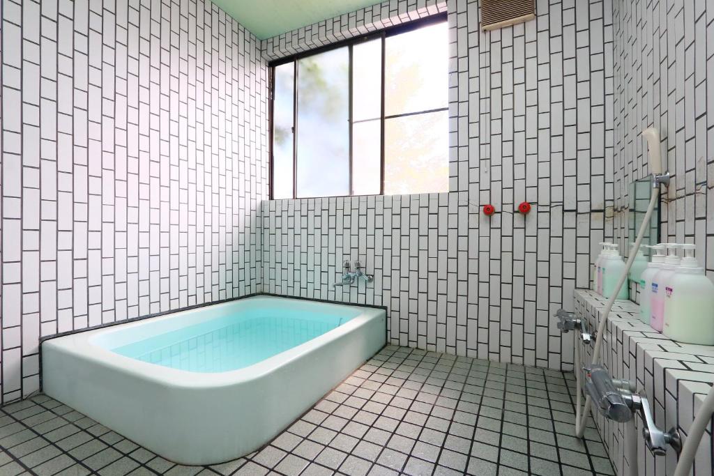 La salle de bains est pourvue de carrelage blanc, d'une baignoire et d'une fenêtre. dans l'établissement Lake Oshino, à Oshino