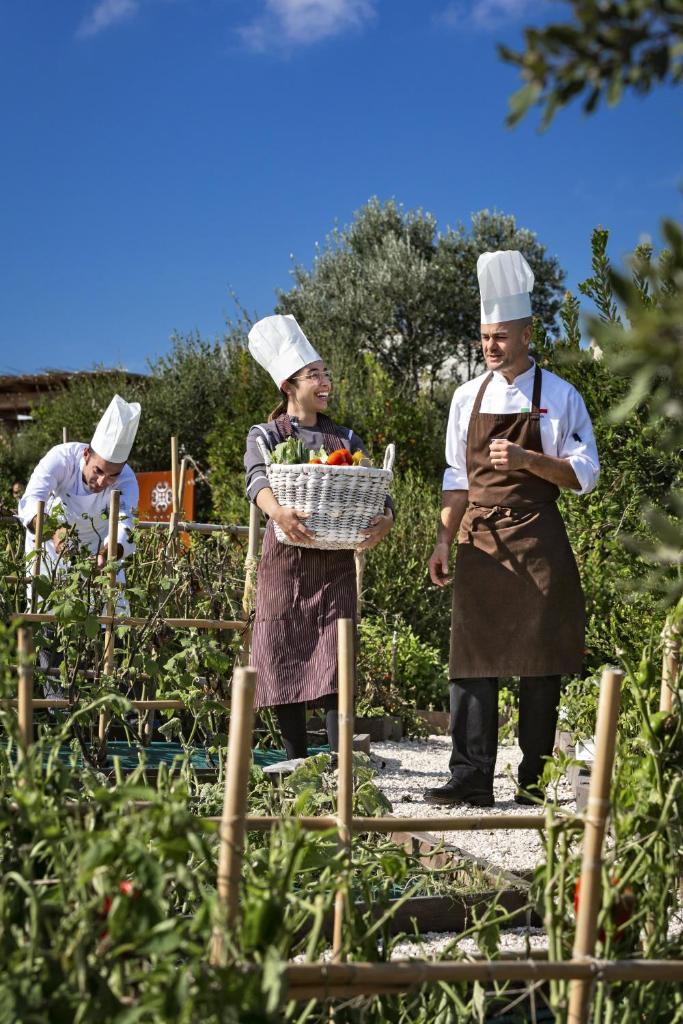 trois personnes dans un jardin avec un panier de légumes dans l'établissement Hotel Li Finistreddi, à Cannigione