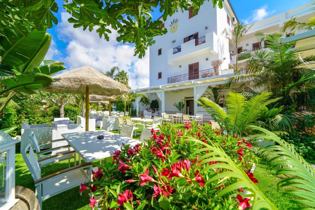 un patio extérieur avec tables, chaises et fleurs dans l'établissement La Bussola Hotel Calabria, à Capo Vaticano