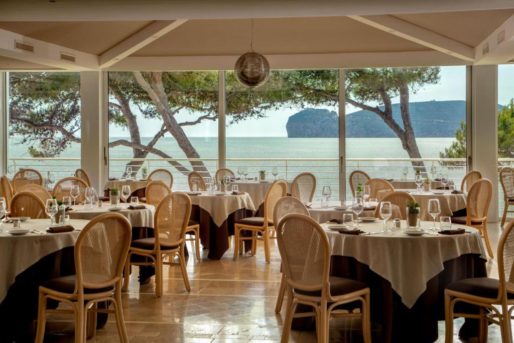 - un restaurant avec des tables et des chaises offrant une vue sur l'eau dans l'établissement El Faro Hotel & Spa, à Porto Conte