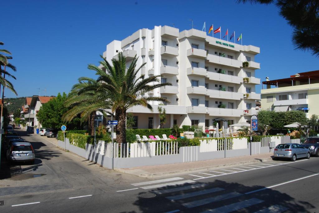 un bâtiment blanc avec des palmiers en face d'une rue dans l'établissement Hotel Costa Verde, à Tortoreto Lido