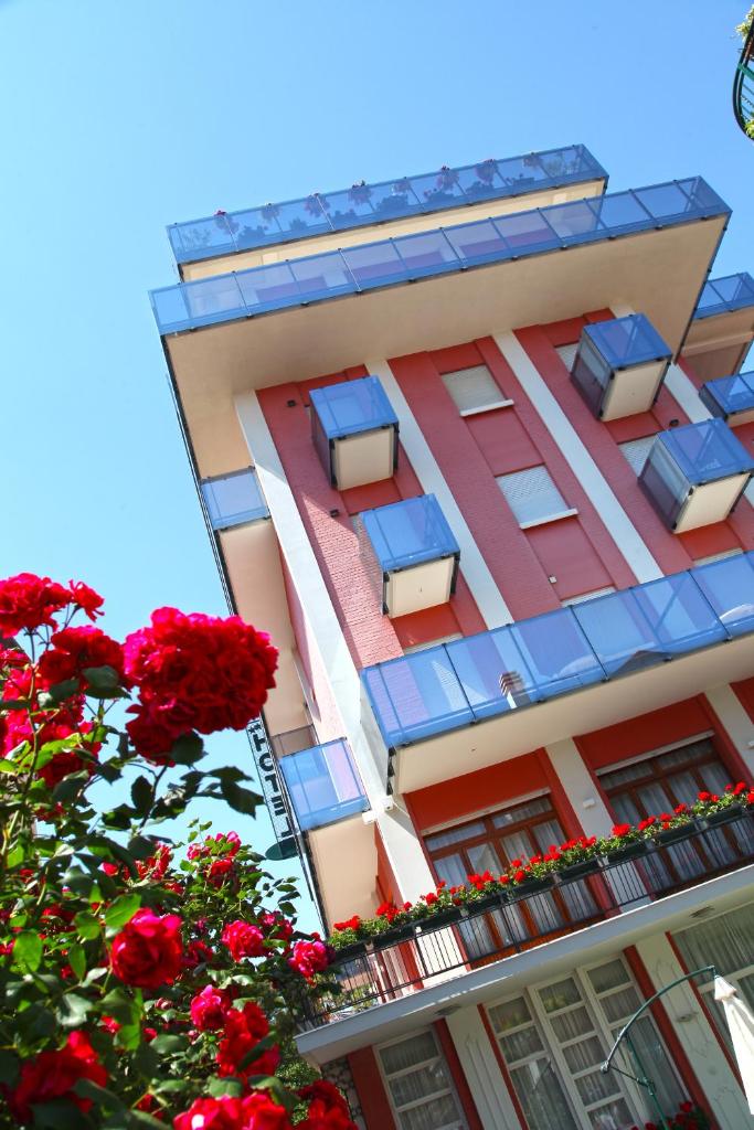 un grand bâtiment avec des fenêtres bleues et des fleurs rouges dans l'établissement Hotel Smeraldo, à Lido di Jesolo