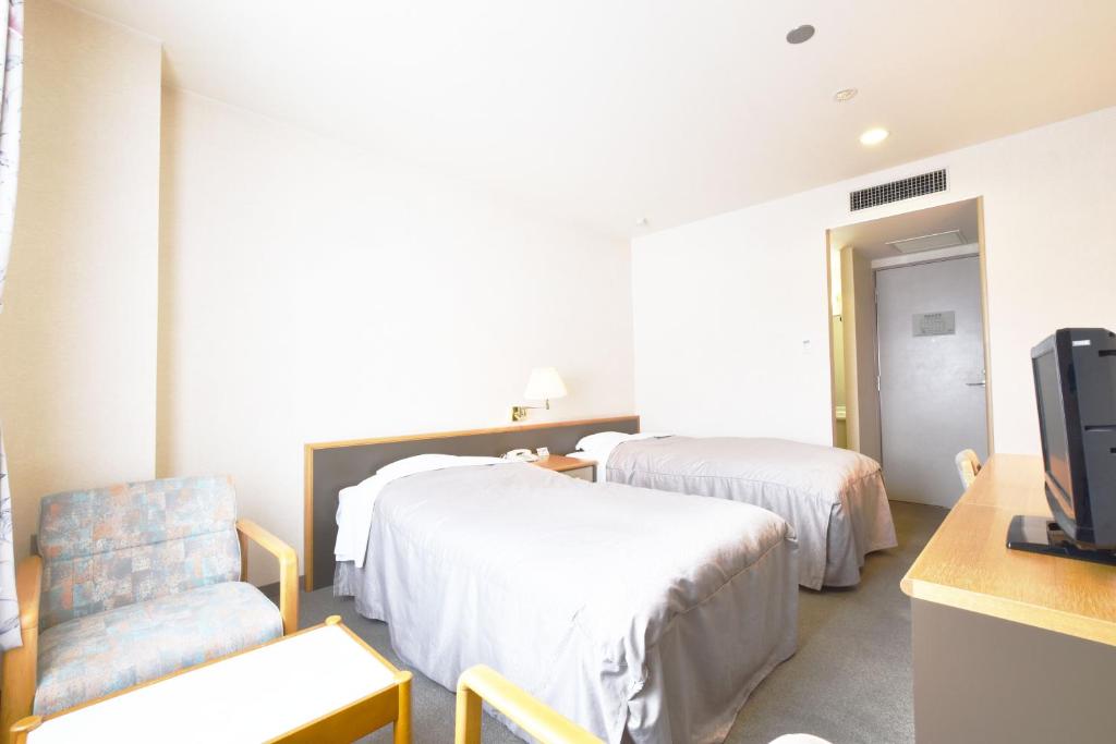 Cette chambre comprend 2 lits, une chaise et une télévision. dans l'établissement Nayoro Onsen Sunpillar, à Nayoro