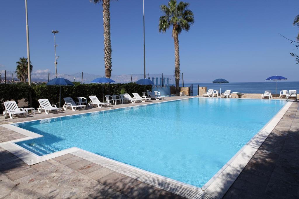 une grande piscine avec chaises et palmiers dans l'établissement Hotel Za Maria, à Santo Stefano di Camastra