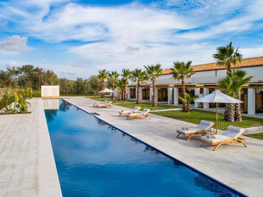 une piscine dans un complexe hôtelier avec chaises et parasols dans l'établissement Il San Corrado di Noto, à Noto