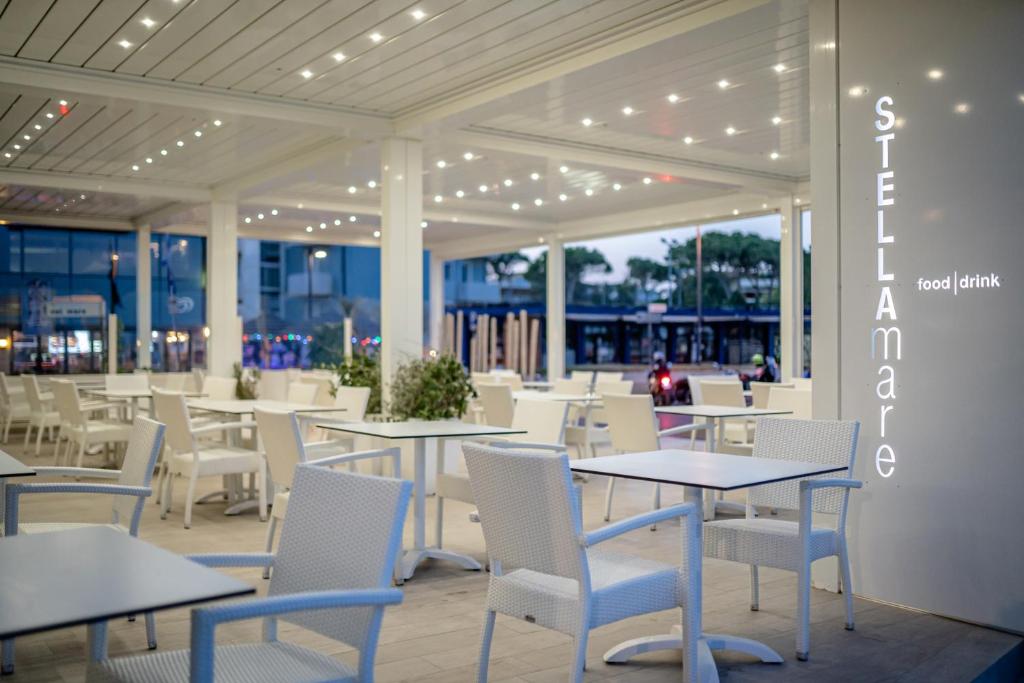 un restaurant avec des tables, des chaises blanches et des lumières dans l'établissement Stellamare, à Caorle