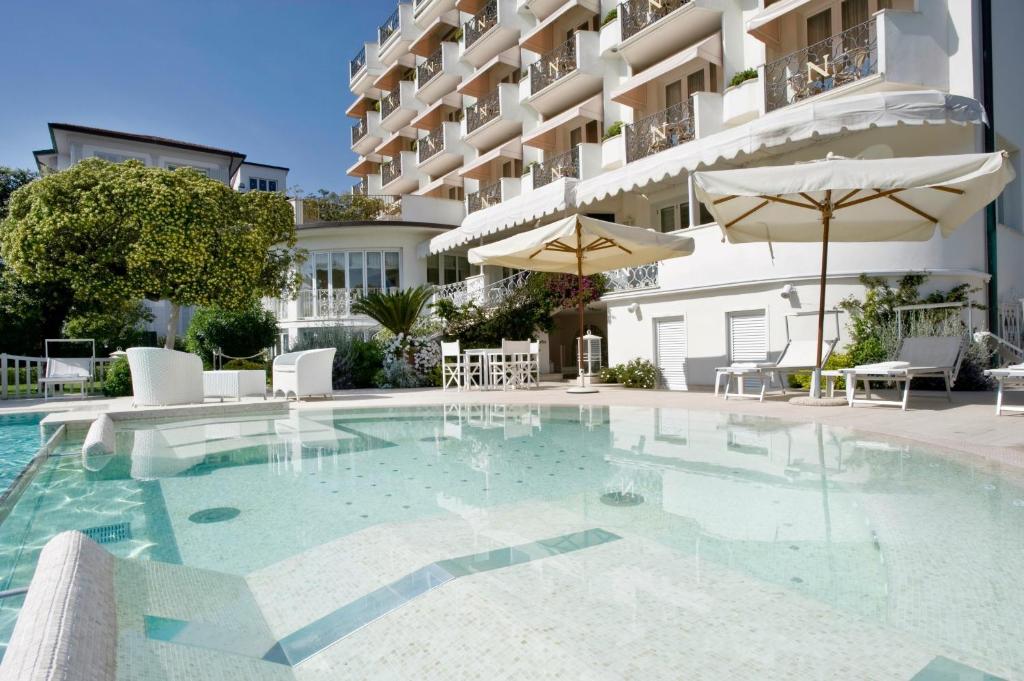 une piscine avec chaises et parasols devant un immeuble dans l'établissement Hotel Il Negresco, à Forte dei Marmi