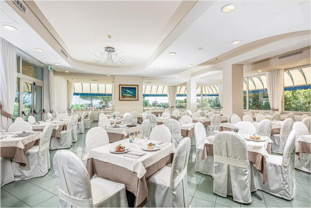 une salle de banquet avec des tables et des chaises blanches dans l'établissement Hotel Bellevue, à Bibione