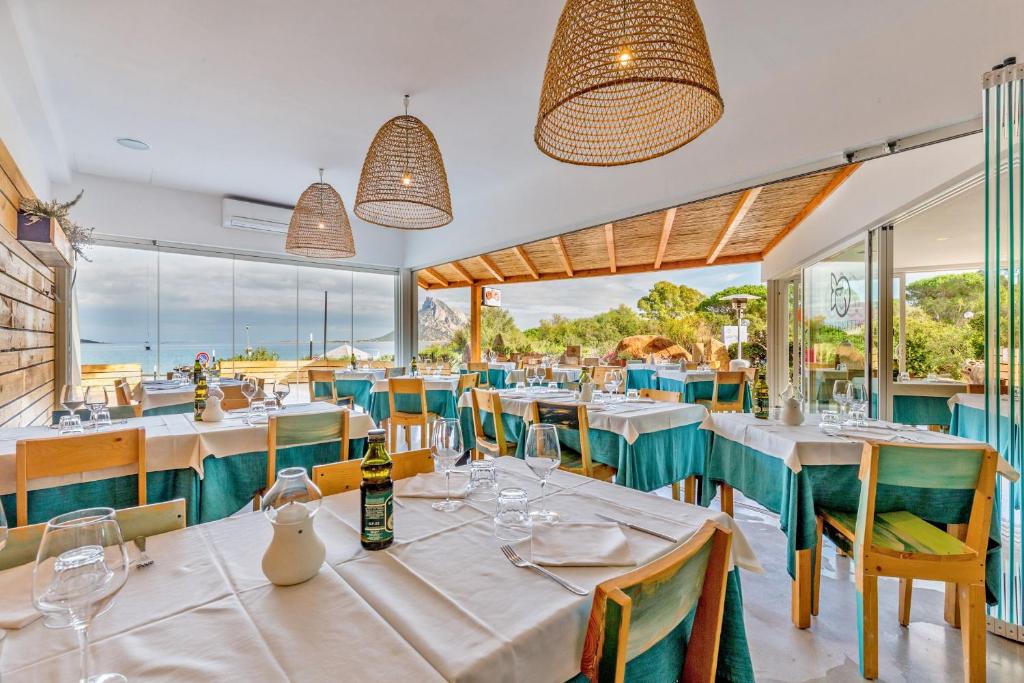un restaurant avec des tables et des chaises blanches et des fenêtres dans l'établissement Residence Hotel Lu Nibareddu, à San Teodoro