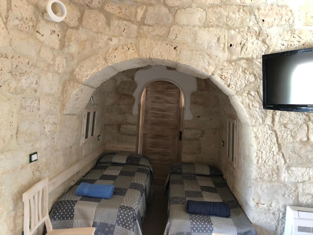 Cette chambre est dotée de 2 lits et d'un mur en pierre. dans l'établissement TRULLO PARCOMONSIGNORE CON PISCINA PRIVATA, à San Vito dei Normanni