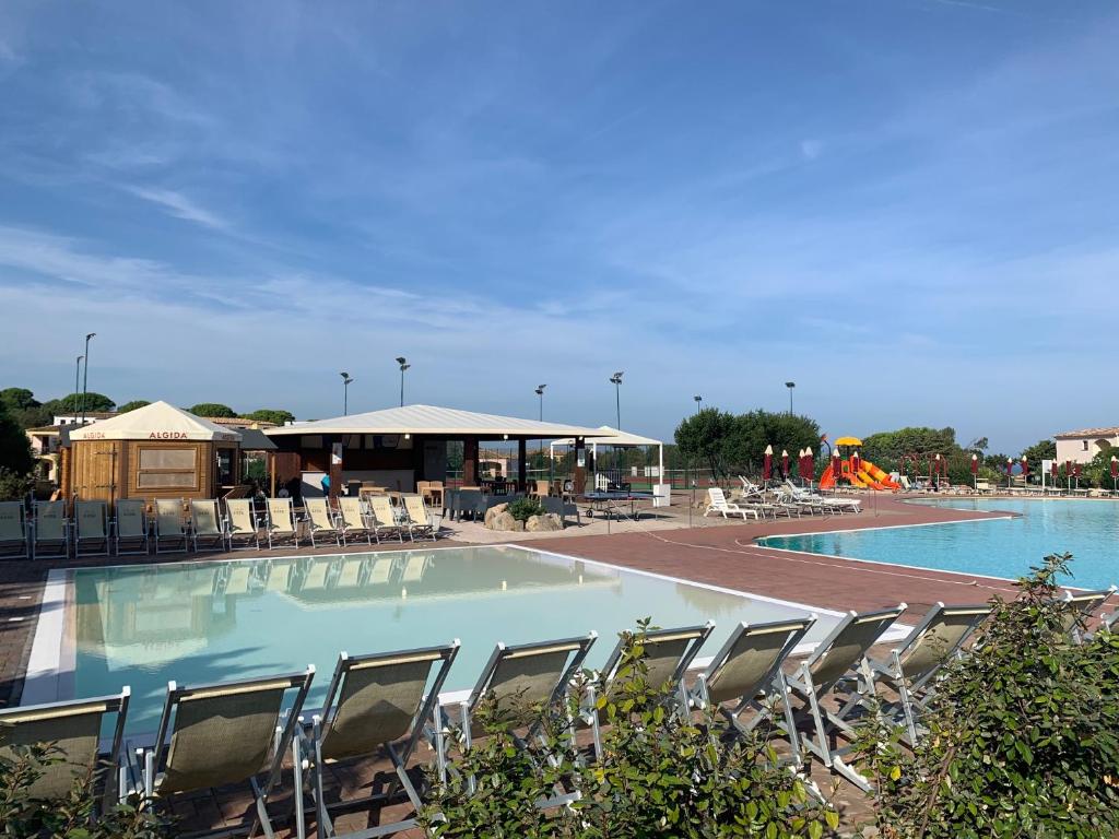 une grande piscine avec des chaises et un bâtiment dans l'établissement Club Esse Gallura, à Aglientu