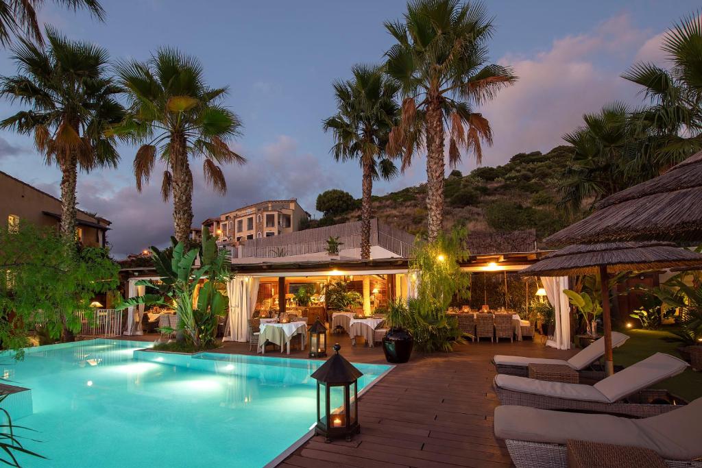 un complexe avec piscine et palmiers la nuit dans l'établissement Boutique Hotel Su Sergenti, à Villasimius